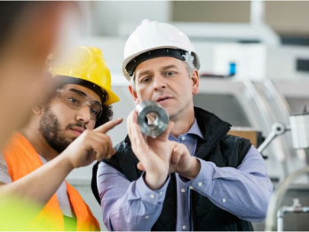 Two employees look at a metal part
