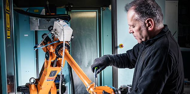 A man works on an orange robotic arm